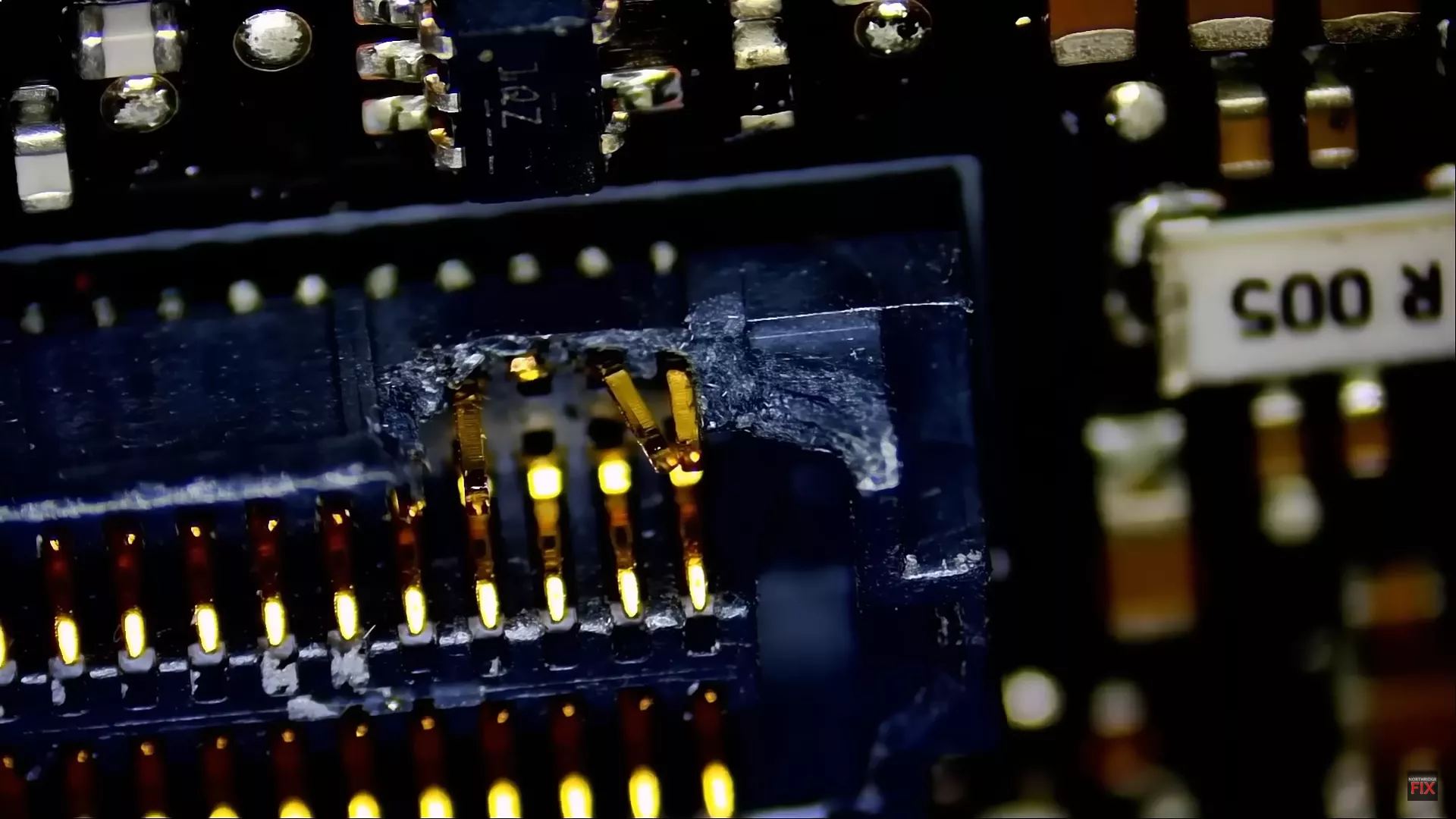Close-up of a damaged circuit board with visible text R 005 and 1AZ.