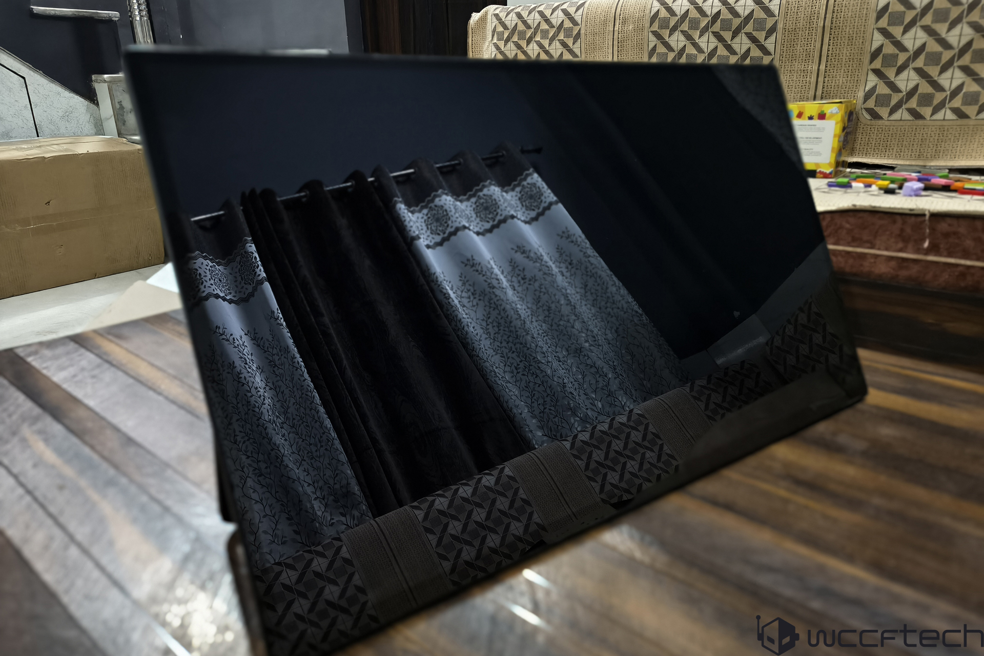 Unbranded glossy screen reflecting patterned curtains and furniture in a living room.