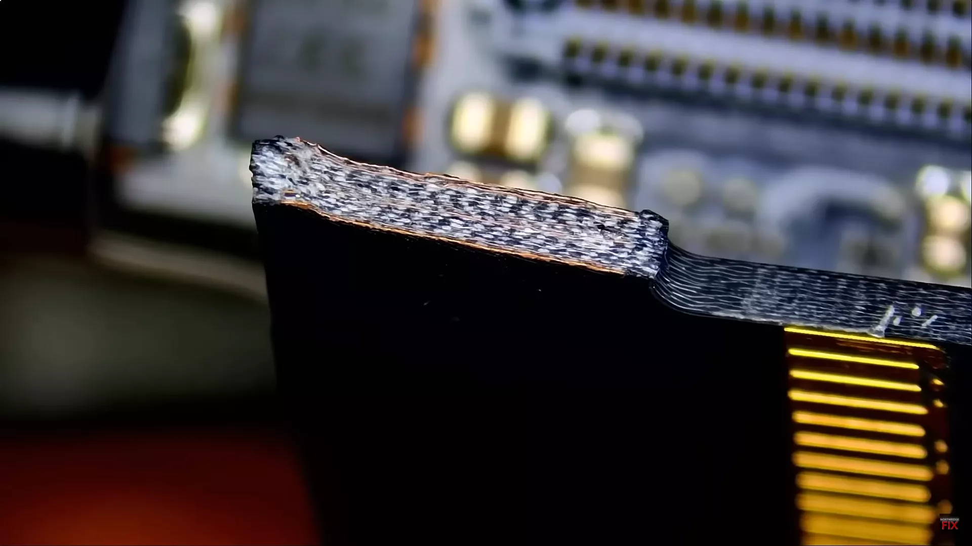 A close-up view of a damaged 12VHPWR connector with exposed wires and frayed edges, seen against a blurred circuit board background.