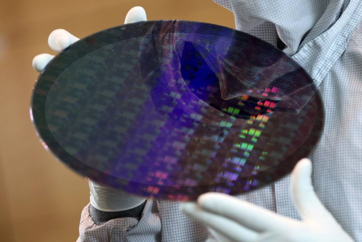 Technician holding a silicon wafer in a cleanroom environment, showcasing microchip technology.