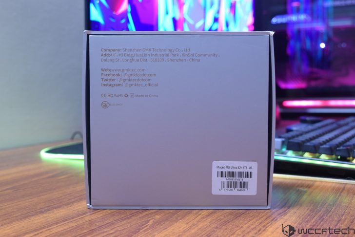 The image shows the back of a box labeled Model: M3 Ultra 32+1TB US with Shenzhen GMK Technology Co., Ltd. details printed, positioned on a desk near a keyboard and monitor with RGB lighting.