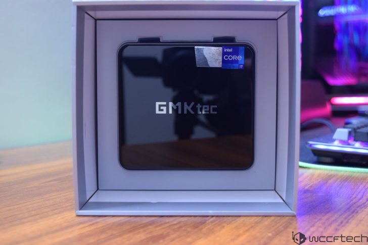 A GMKtec mini PC with 'Intel Core i7' branding is displayed in a box on a wooden table.