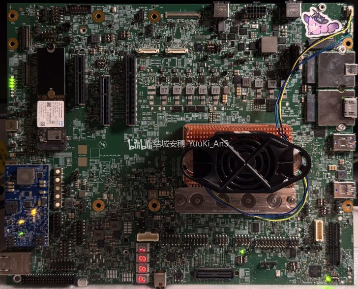 A detailed view of an unbranded circuit board with multiple components including a prominent fan and heat sink, glowing indicator lights, a 'BiliBili' logo, and a colorful sticker in the corner.