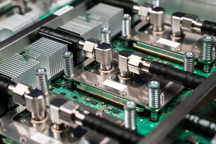 A close-up of a server motherboard showing metallic cooling blocks, heat sinks, and connected pipes for liquid cooling.