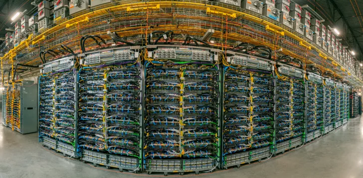 A large room filled with rows of server racks intricately connected by numerous colored cables.
