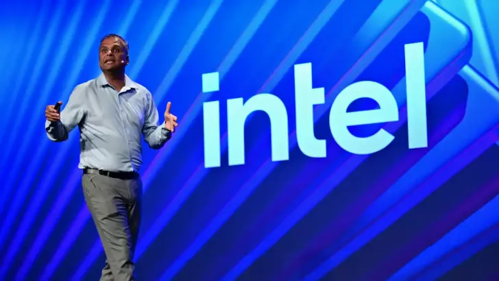 A presenter stands on stage in front of a large 'Intel' logo with a blue background.