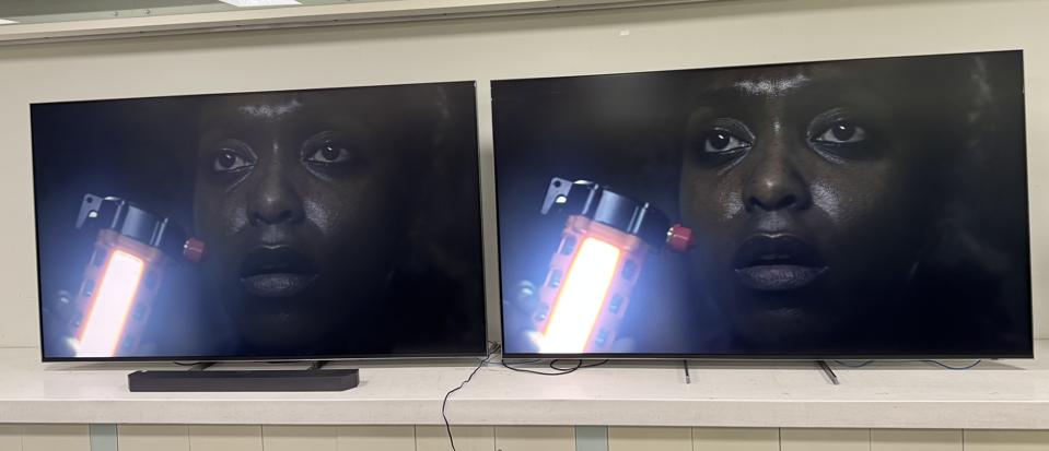 Two televisions side by side display a close-up scene from a movie or game featuring a character holding a glowing device, showcasing color and contrast differences.