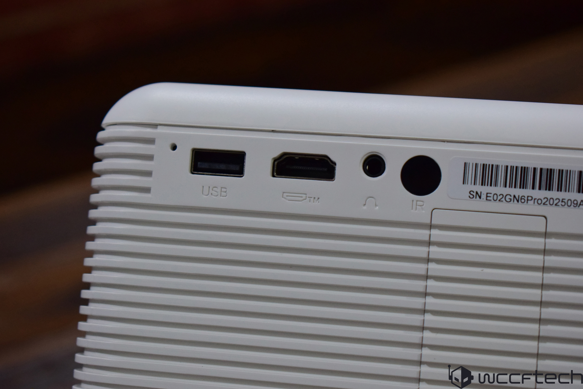 A close-up of a white electronic device showing a 'USB' port, an HDMI port, a headphone jack, and an IR sensor, with a visible serial number 'SN: E02GN6Pro202509A9Q'.