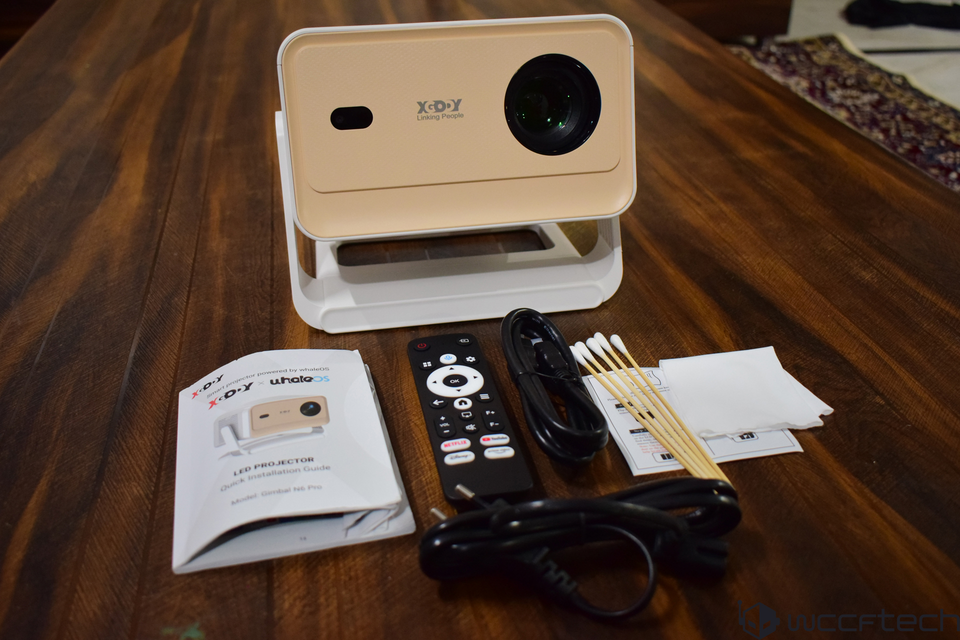 A beige XDY LED projector is displayed on a stand with its remote control, cables, cotton swabs, cleaning cloths, and a user manual titled 'LED Projector Quick Installation Guide Model: Gimbal N6 Pro'.