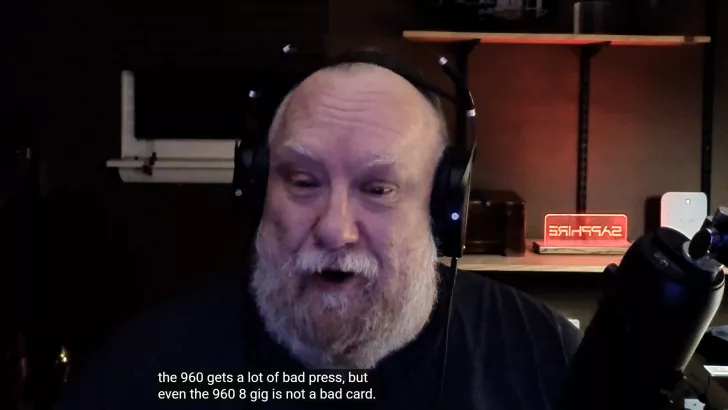 A person with headphones is speaking into a microphone, with a shelf displaying a neon sign with the word 'SAPPHIRE' in the background, and subtitles on-screen read, the 960 gets a lot of bad press, but even the 960 8 gig is not a bad card.