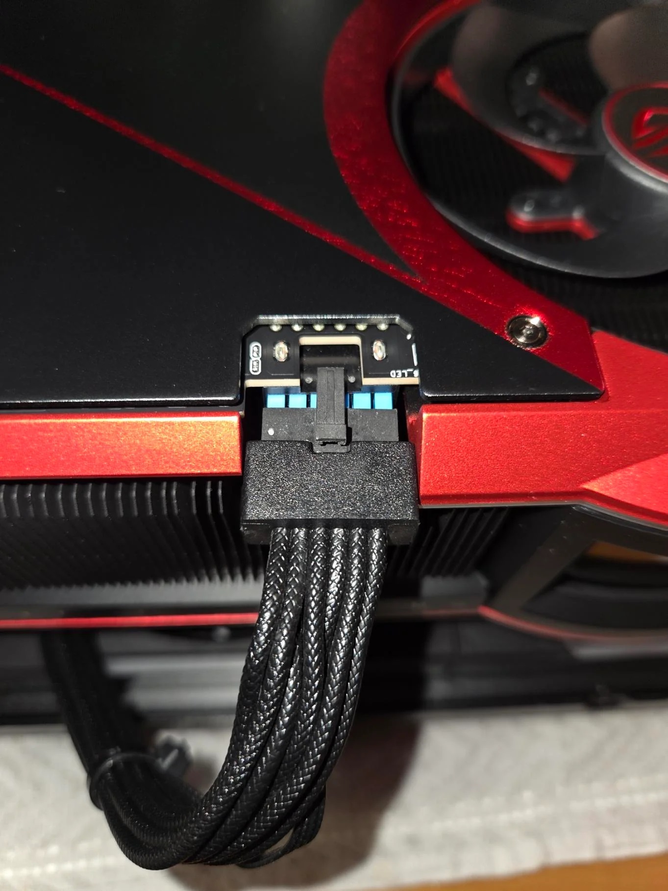 A close-up of a red graphics card's power connector labeled 'LED CST,' showing its cable connection.
