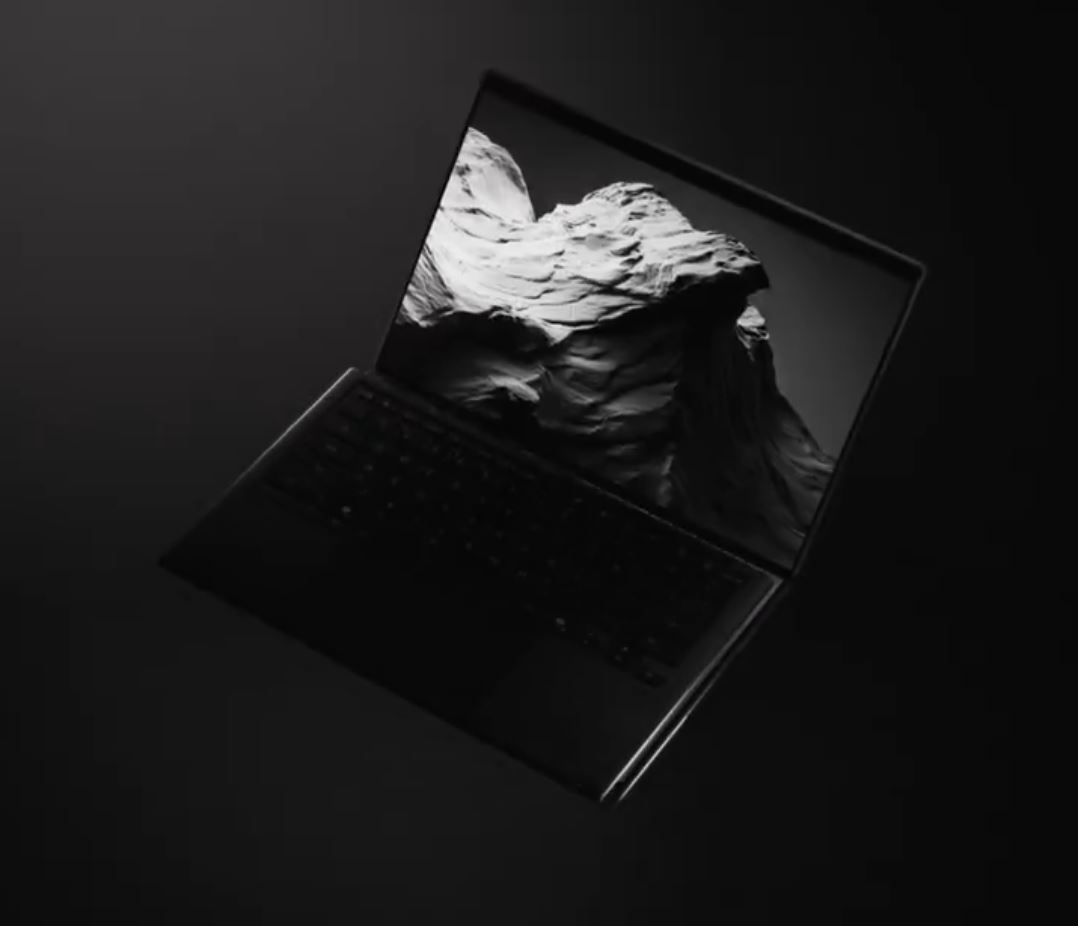 A sleek unbranded laptop in a dimly lit setting displays a monochrome landscape image on its screen.