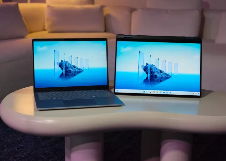 Two HP laptops are displayed on a table, with one in a standard format and the other in tent mode, both showing a wallpaper of floating glass panels in water.