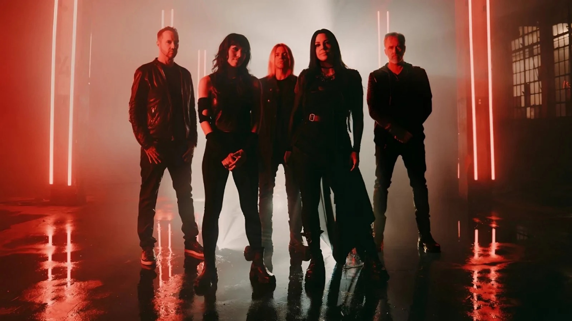 A group of five people standing in a dimly lit, red-tinted room with reflective floors and vertical light bars in the background.