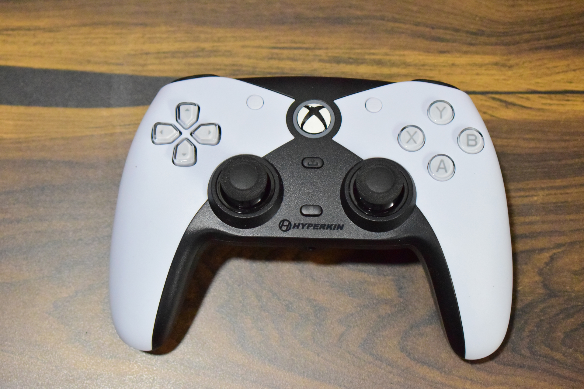 A white and black Hyperkin controller with Xbox button layout rests on a wooden surface.