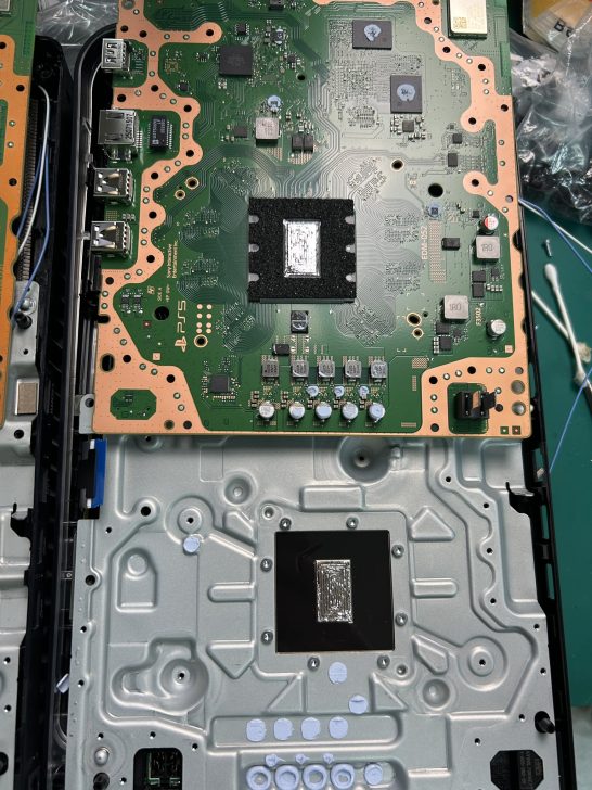A PlayStation 5 circuit board exposed, with visible HDMI and USB ports and thermal paste applied on the main processor.