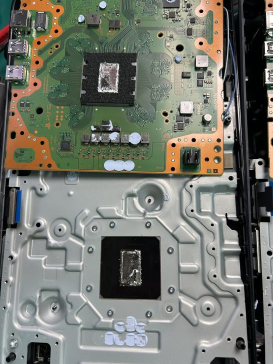 The internal components of a PlayStation 5, with a detailed view of its circuit board and chip placement.