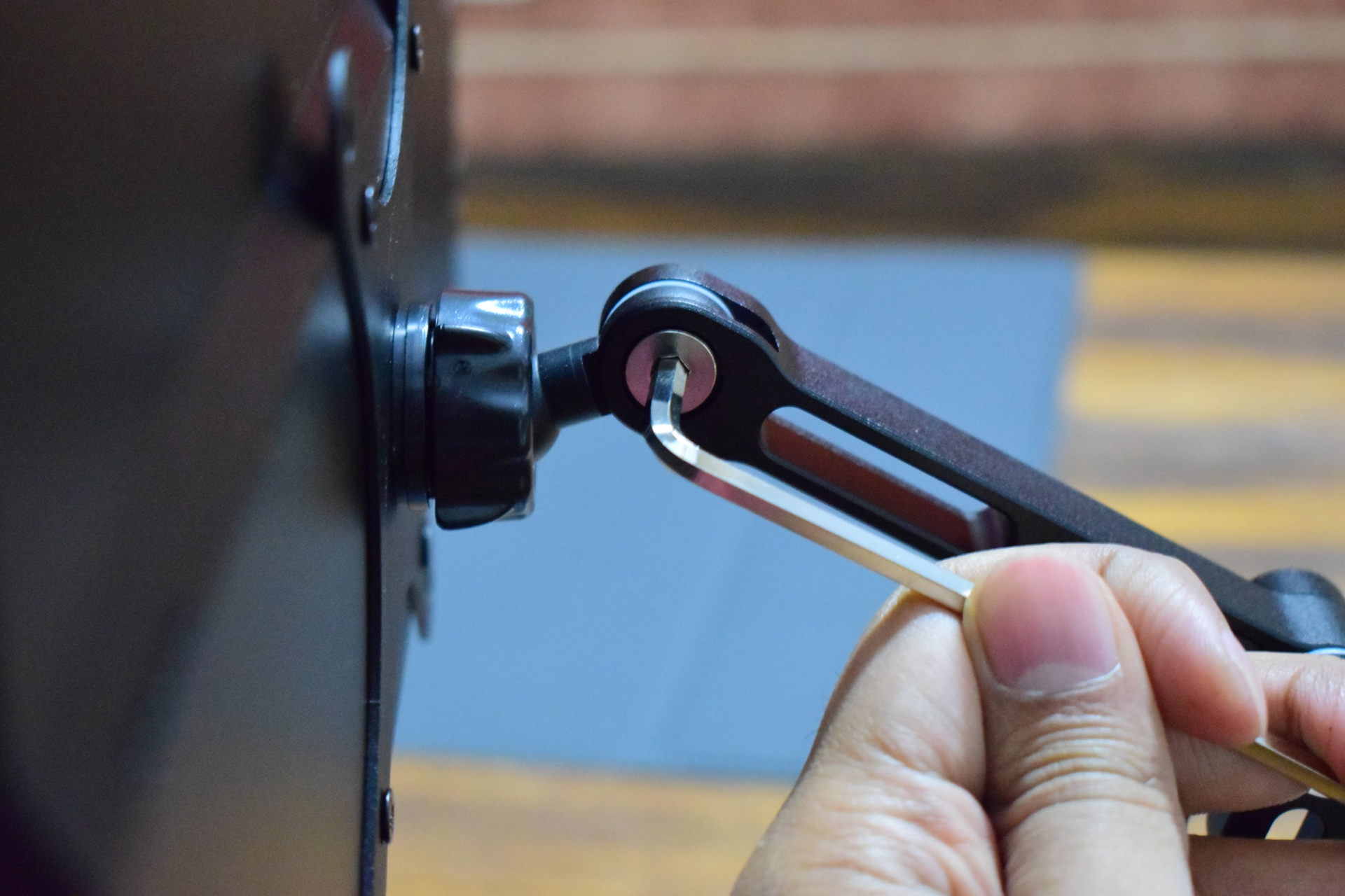 A close-up of a hand using an Allen wrench to adjust a bolt on a television wall mount bracket.