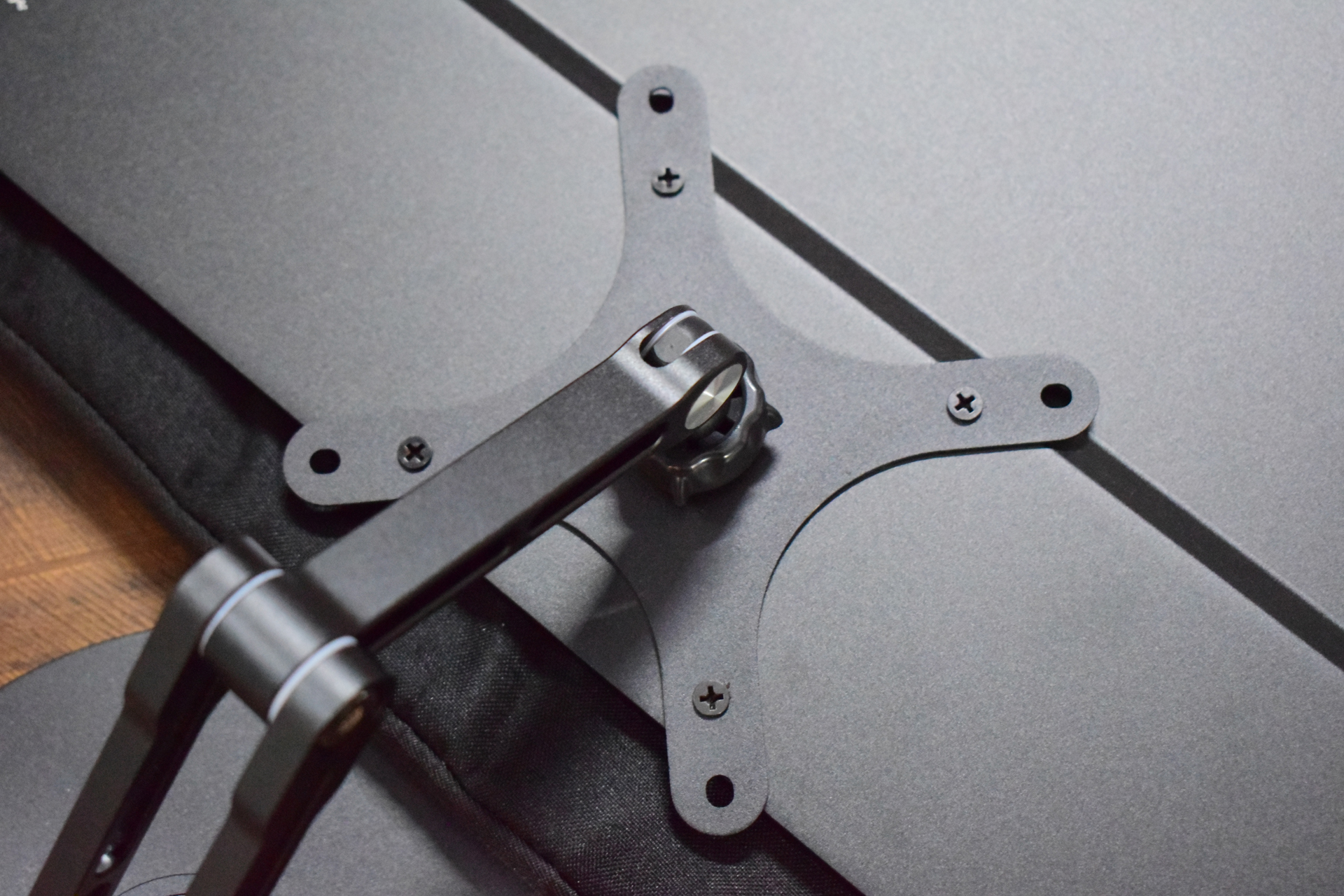 A VESA mount bracket attached to a monitor stand arm on a dark surface.