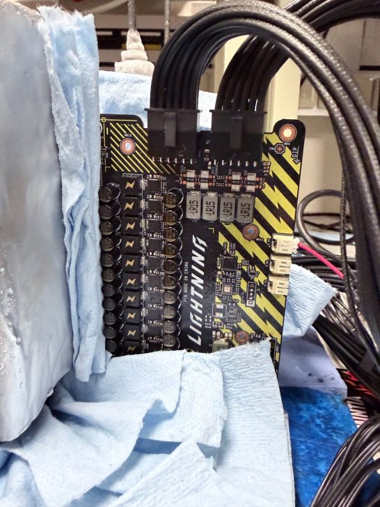 A close-up of an MSI Lightning graphics card component with visible capacitors, labeled 'MADE IN CHINA', surrounded by cables and blue coolant-soaked material.