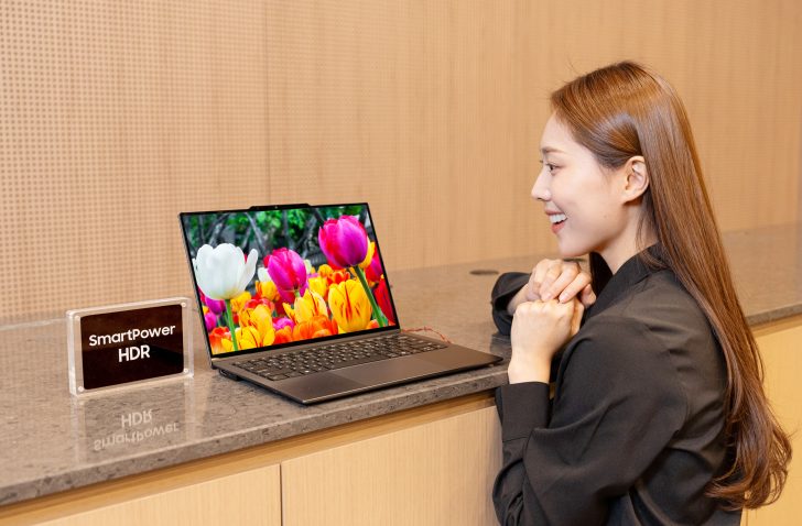 A woman smiles at a laptop displaying colorful tulips next to a sign reading 'SmartPower HDR'.